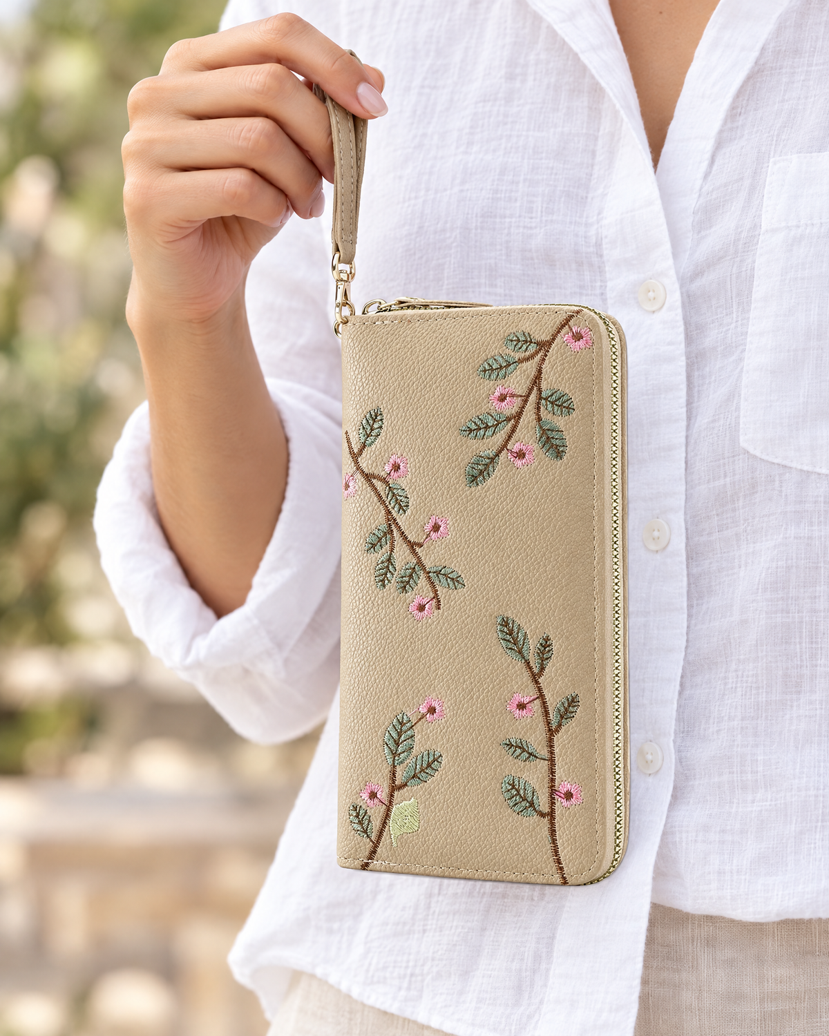 Hand holding khaki embroidered floral wristlet wallet